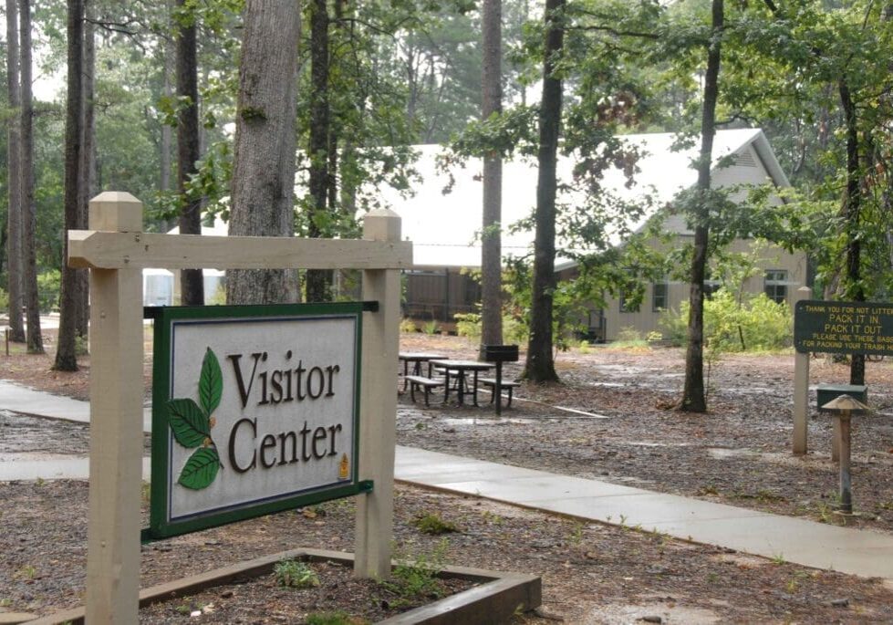 A sign for the visitor center in front of some trees.